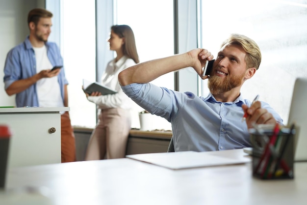 Foto uomo d'affari casuale che lavora alla scrivania dell'ufficio, utilizzando il telefono cellulare e il laptop