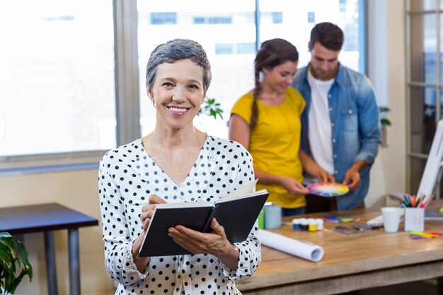 Casual businesswoman writing in diary while colleagues working in the office