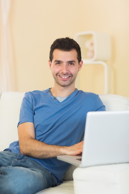 Casual cheerful man sitting on couch using laptop