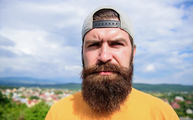 Casual chic Cool hipster Bearded man in fashion hipster cap outdoor Brutal man with long beard and mustache Hipster in street fashion wear on summer landscape