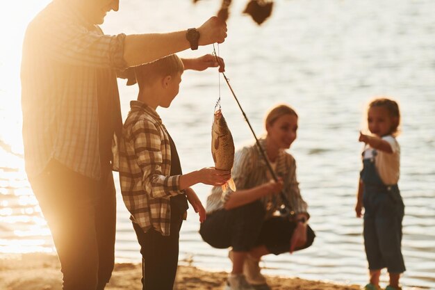 Photo in casual clothes father and mother with son and daughter on fishing together outdoors at summertime