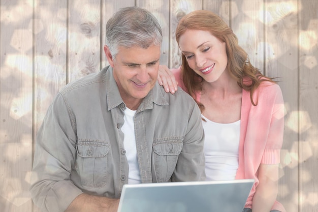 Casual couple looking at laptop against light glowing dots design pattern