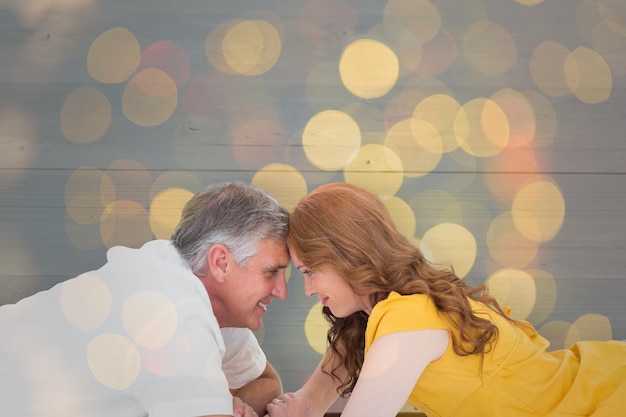 Casual couple lying on floor with piggy bank against close up of christmas lights