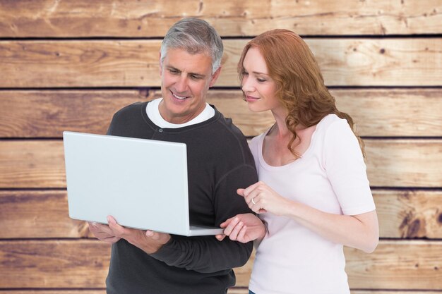 Casual couple using laptop together against wooden planks background