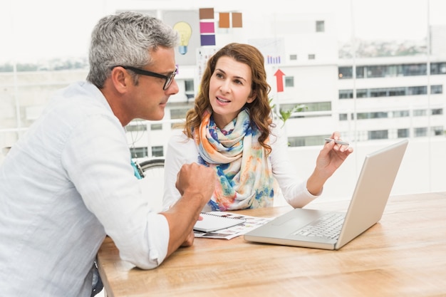 Progettisti casuali che discutono e che lavorano con il computer portatile