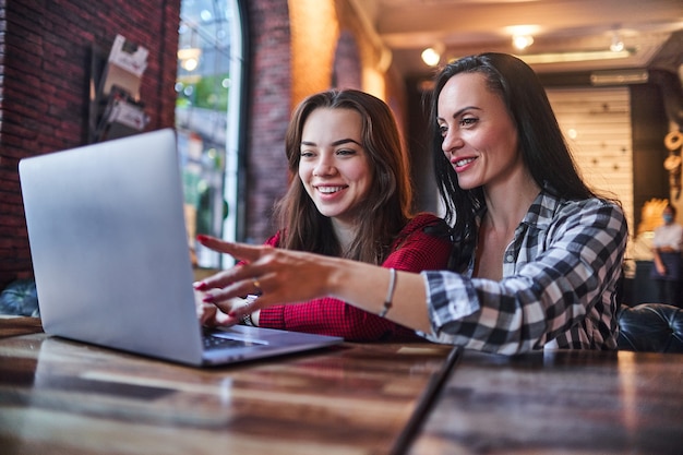 Casual happy smiling mother and daughter watching together video content on a laptop and having good time together in a coffee shop