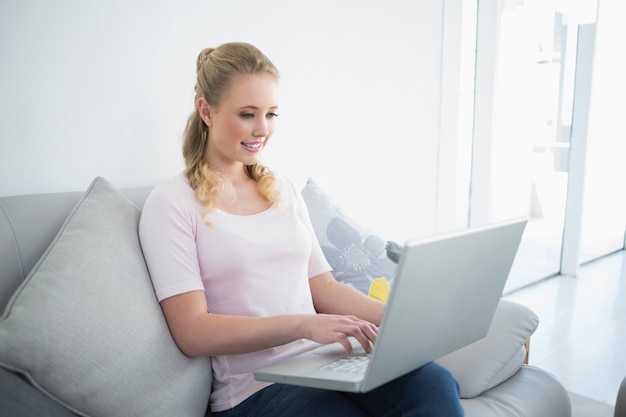 Casual inhoud blonde zittend op de bank met behulp van laptop