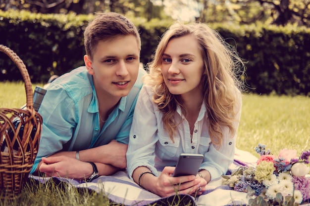 Casual jong koppel ontspannen op een gazon en op zoek naar foto's op smartphone.