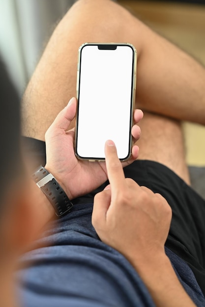 Casual jonge man zit op de bank tekst te typen en chatten met vrienden op de mobiele telefoon
