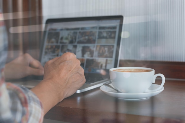 Casual man browsing internet on laptop computer with cup of coffee on table at coffee shop