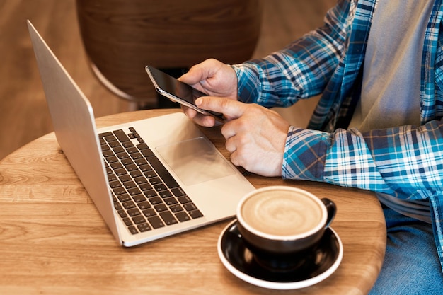 Libero professionista uomo casual che lavora online con macbook e telefono cellulare e beve caffè mattutino