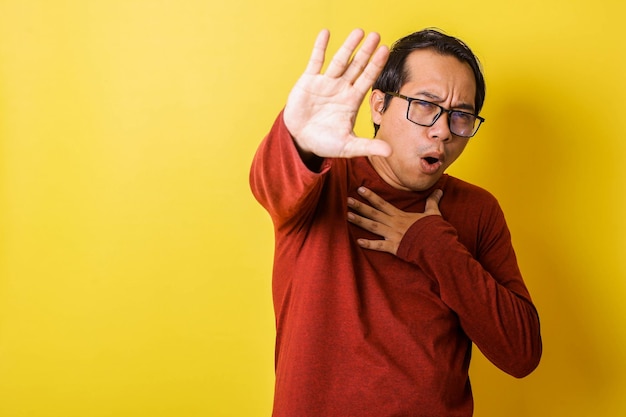 Casual man in glasses holding his chest with stop hand gesture
isolated on yellow background