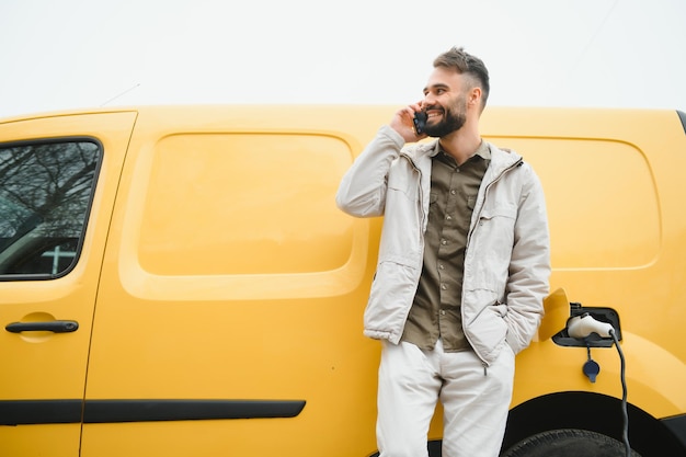 Casual man in de buurt van elektrische auto die wacht op het einde van het oplaadproces van de batterij