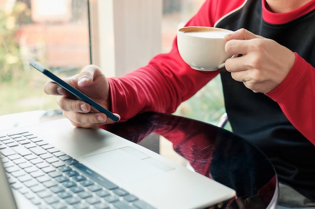 Foto casual man koffie drinken met behulp van smartphone en laptop op tafel