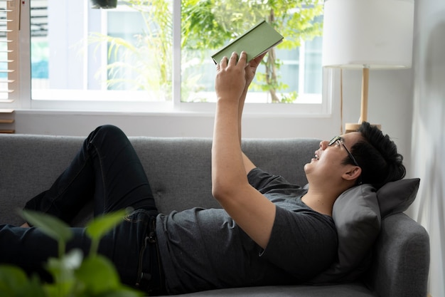 Casual man lying on comfortable sofa and reading book.