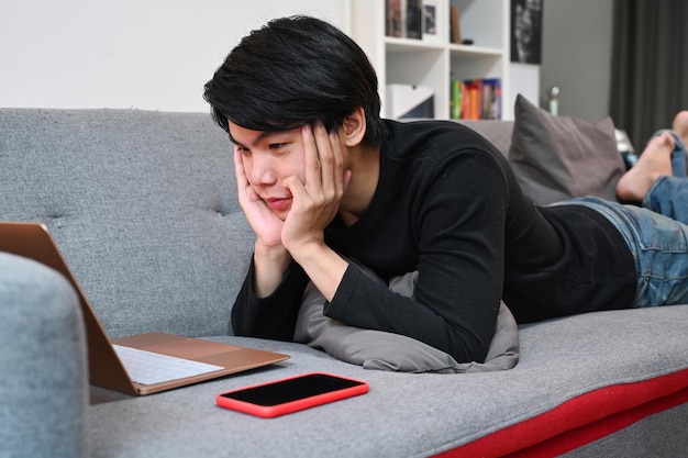 Casual man lying on sofa and xAwatching something on laptop