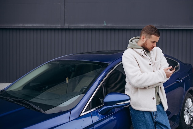 Casual man met smartphone in de buurt van elektrische auto die wacht op het einde van het oplaadproces van de batterij