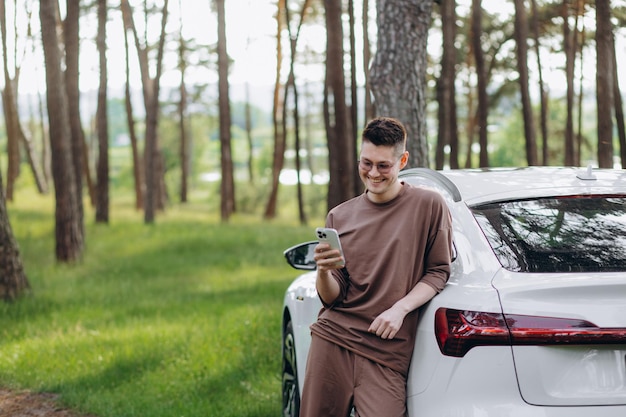 Casual man met smartphone in de buurt van elektrische auto die wacht op het einde van het oplaadproces van de batterij