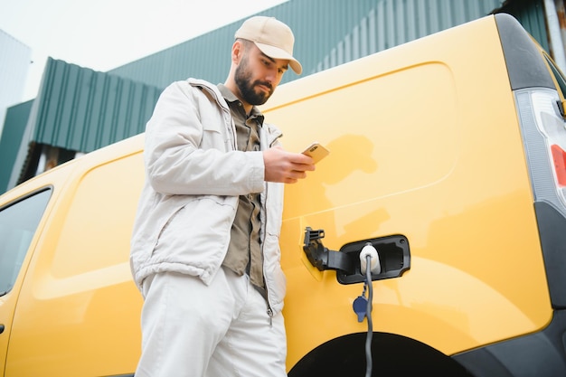 バッテリー充電プロセスの終了を待っている電気自動車の近くのカジュアルな男