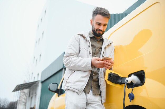 バッテリー充電プロセスの終了を待っている電気自動車の近くのカジュアルな男