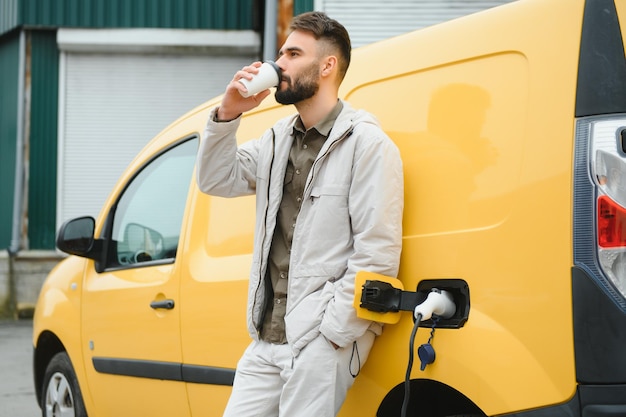 バッテリー充電プロセスの終了を待っている電気自動車の近くのカジュアルな男