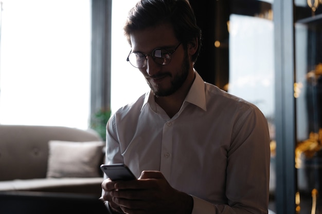 Casual man ontspannen met behulp van slimme telefoon, jonge man browsen op smartphone in café interieur.