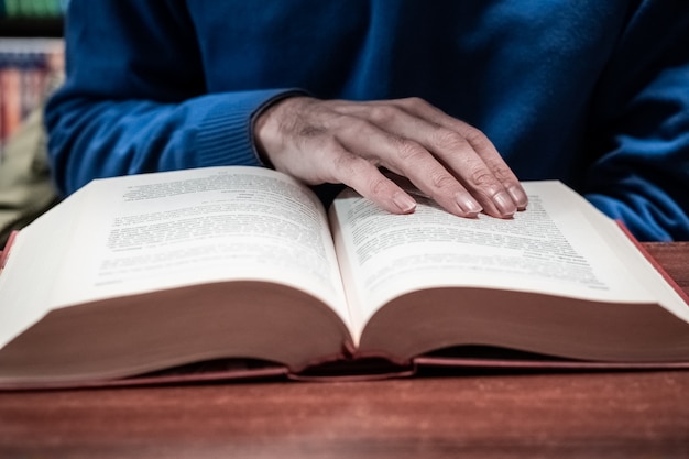 Libro di lettura casuale dell'uomo sulla tavola di legno in biblioteca, stile d'annata