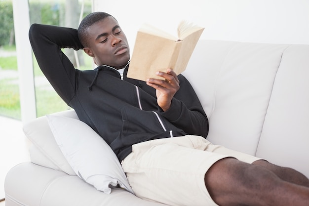 Casual man sitting on his sofa reading a book