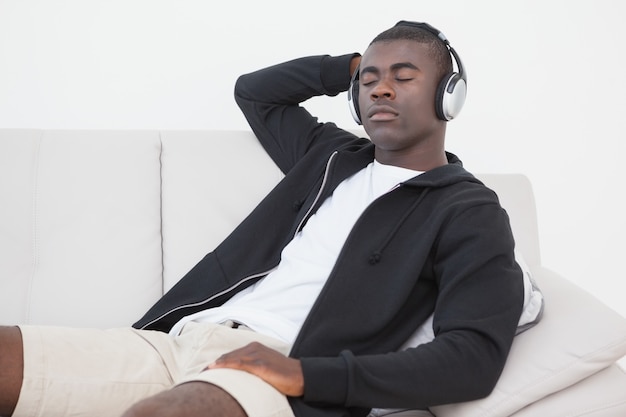 Casual man sitting on sofa enjoying music with eyes closed at home in the living room