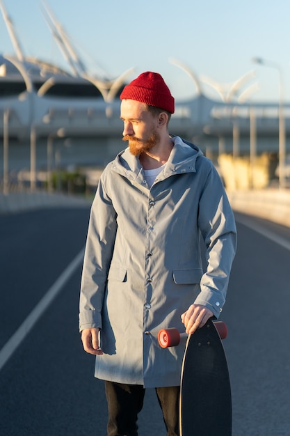 Uomo casual con longboard sulla città edificio hipster elegante skateboarder tenere skateboard sul tramonto