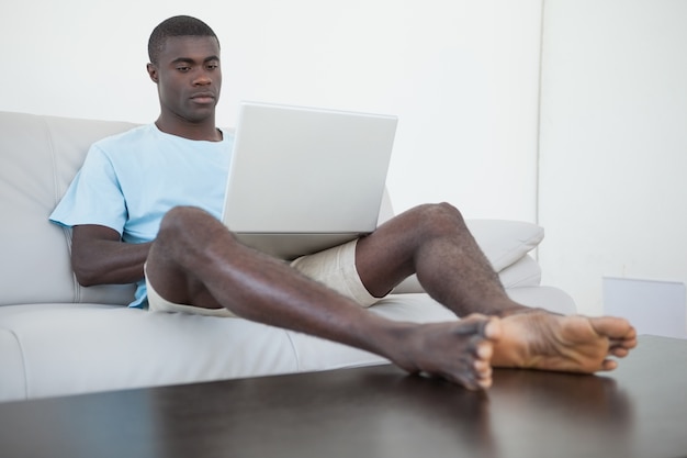 Casual man zittend op de bank met behulp van laptop met de voeten omhoog