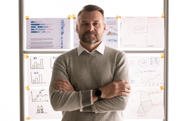 Photo casual mature businessman crossing arms by chest while standing against whiteboard with documents