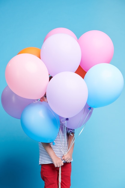 Casual meisje gluren door klein gaatje tussen kleurrijke ballonnen terwijl ze een heleboel voor haar gezicht houdt