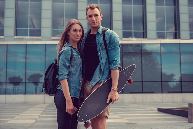 Casual paar met longboard poseren op een plein in een stad.