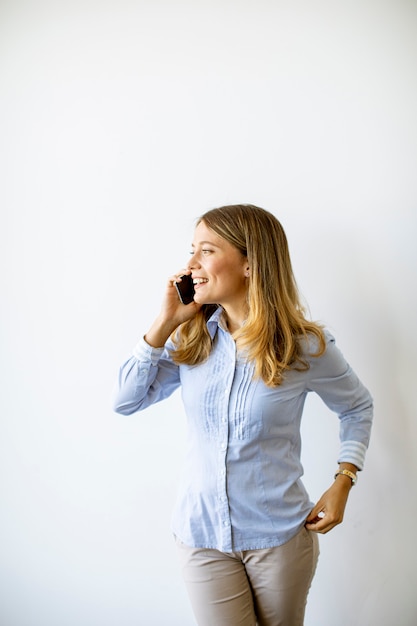 Foto casual piuttosto giovane donna d'affari in piedi dal muro in ufficio e utilizzando il telefono cellulare