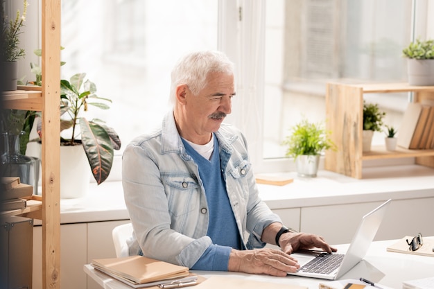 Casual senior kantoormedewerker concentreren op het analyseren van online gegevens zittend door bureau achter laptop