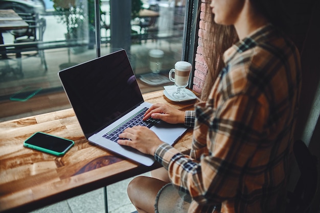 Casual smart modern woman freelancer remotely working at a laptop in a coffee shop. Cozy workplace