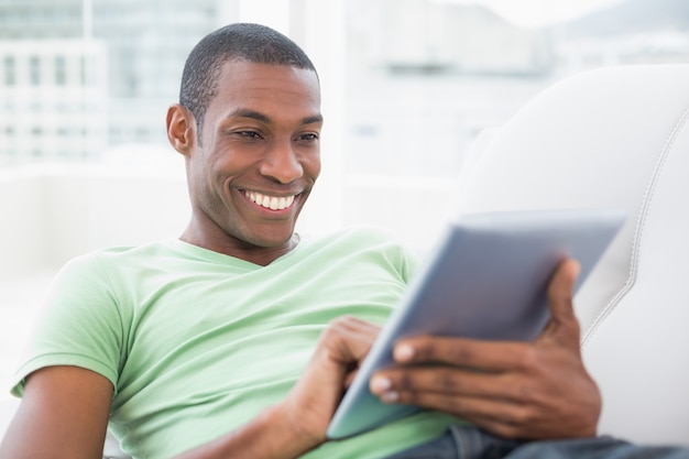 Casual smiling Afro man using digital tablet on sofa