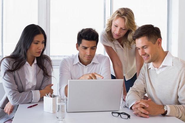 Casual smiling business team having a meeting using laptop