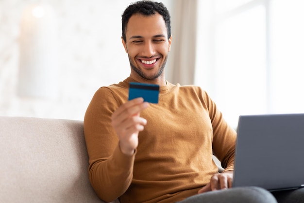 Casual smiling man using pc and credit card at home