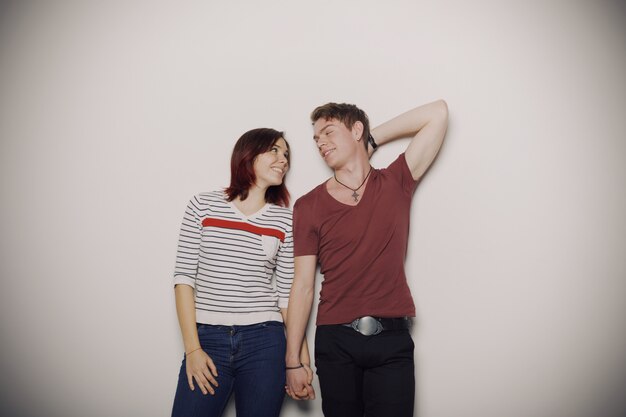 Casual smiling young couple posing over creme wall