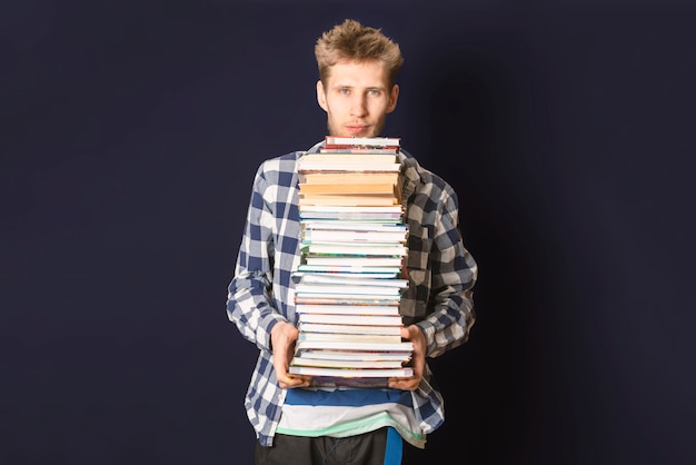 Casual student carry huge stack of books on dark background f
