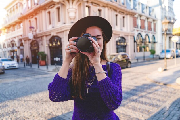 ヨーロッパの都市を旅行中に写真を撮るデジタル一眼レフカメラで帽子のカジュアルなスタイリッシュな女性写真家