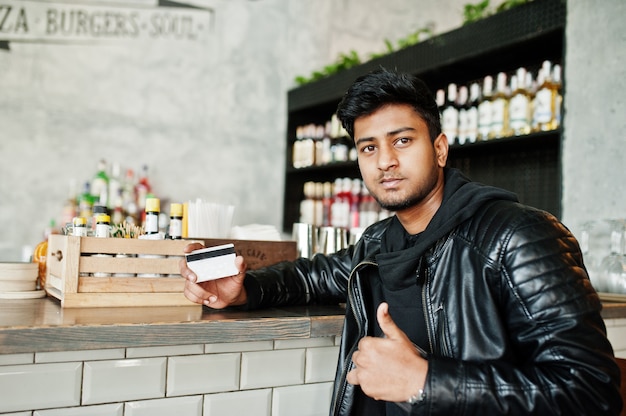 Casual and stylish young asian man wear on leather jacket sitting on bar and holding credit card for pay