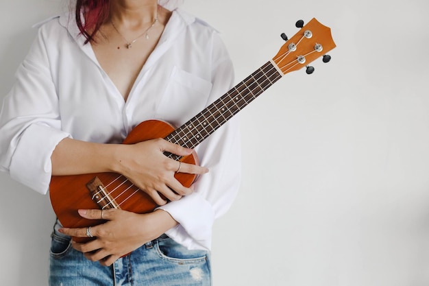 Casual and stylish young girl in white shirt hold ukulele\
guitar with copy space for art and musical