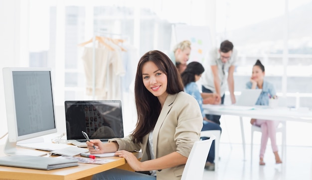 Casual woman at desk with colleagues behind in office