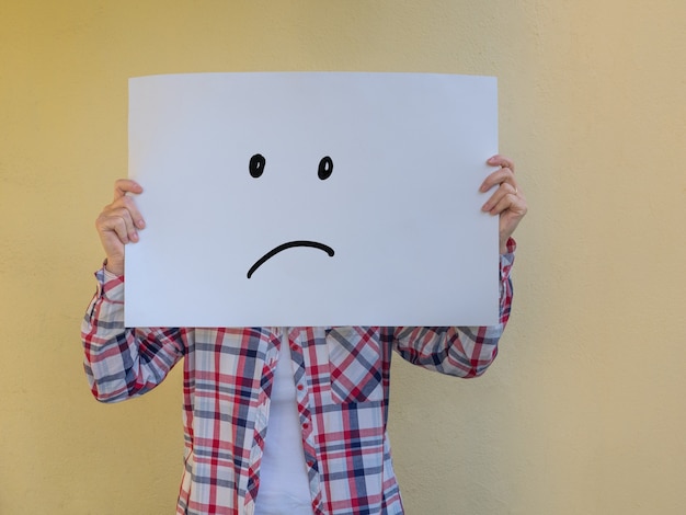 Casual woman hiding her face behind a blank billboard with an angry face Copy space