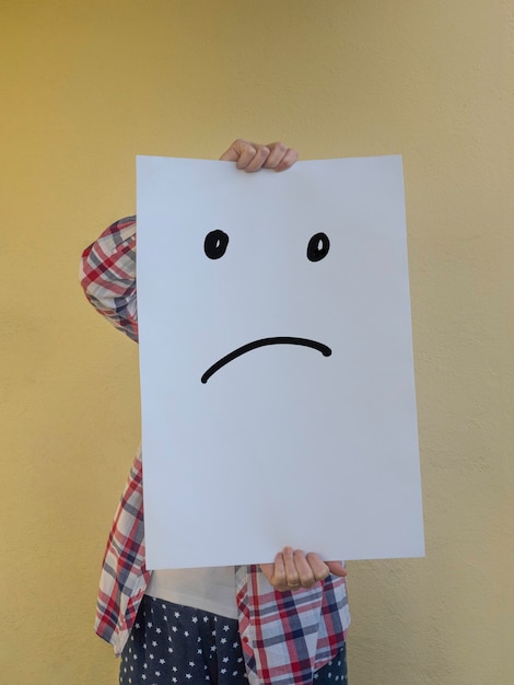 Casual woman hiding her face behind a blank billboard with a sad face Copy space