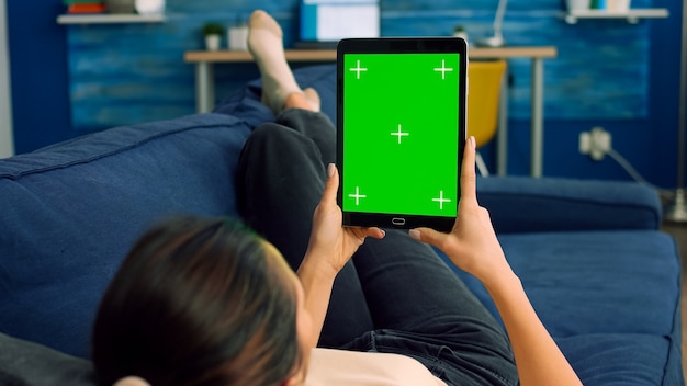 Casual woman lying on sofa using tablet computer green screen chroma key in vertical portrait mode