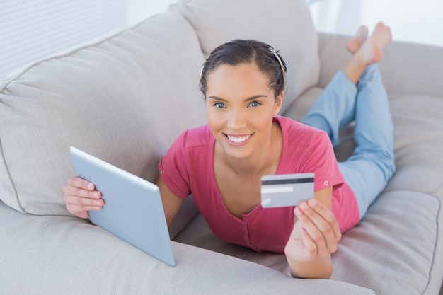 Casual woman lying with a credit card and a tablet